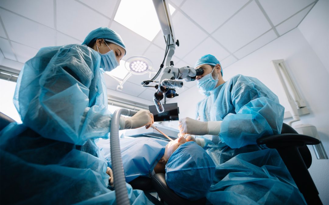 A team of oral and maxillofacial surgeons at River Ridge Oral Surgery utilizing an advanced surgical microscope for a high-precision apicoectomy or complex root canal surgery in a sterile environment.