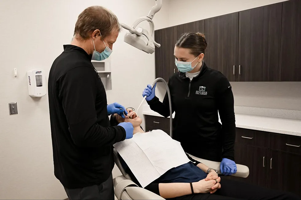 A professional oral surgeon and assistant performing a surgical tooth extraction or wisdom teeth removal surgery using advanced clinical techniques at River Ridge Oral & Maxillofacial Surgical Center.