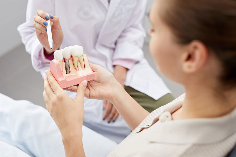 An oral and maxillofacial surgeon at River Ridge Oral Surgery using a detailed cross-section model to explain the components of dental implant surgery, including the post and abutment, to a patient.