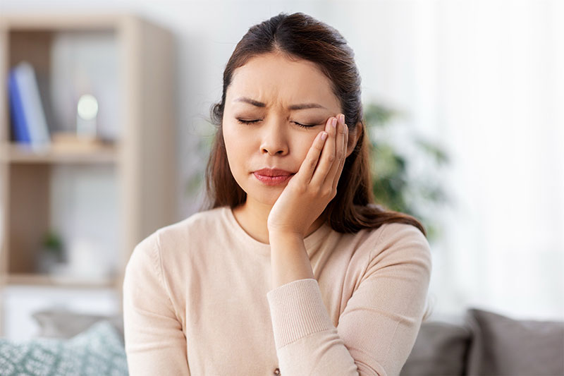 A woman at home experiencing a severe toothache, potentially requiring emergency tooth pain relief or a consultation for impacted wisdom teeth removal at River Ridge Oral & Maxillofacial Surgical Center.