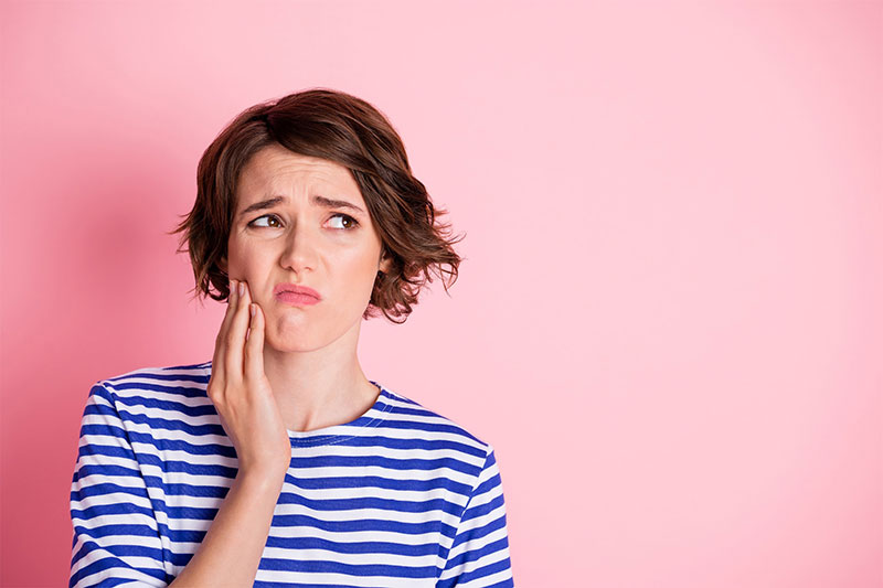 A person experiencing facial discomfort or swelling, signaling a potential need for an emergency dental visit or a consultation for impacted wisdom teeth removal at River Ridge Oral & Maxillofacial Surgical Center.
